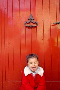 Petite fille tire la langue devant une porte rouge
