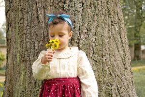Petite fille au bouquet de pissenlits devant un arbre